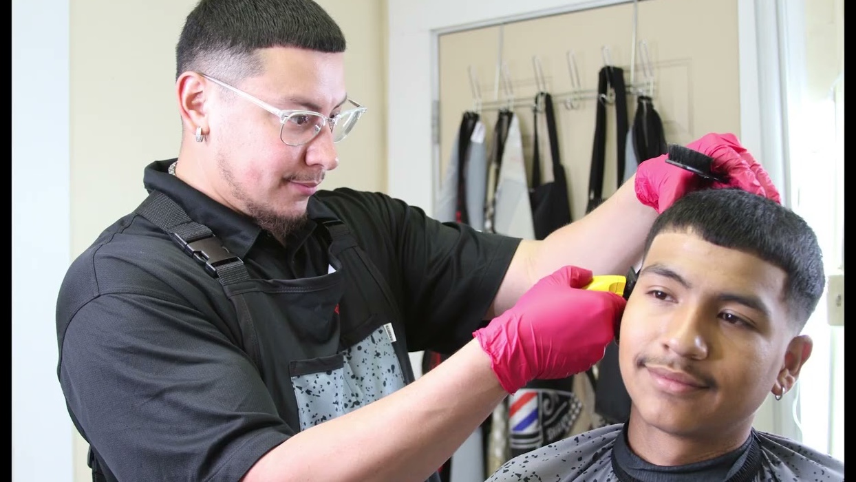 A barber cutting a student's hair at AGORA Barber College